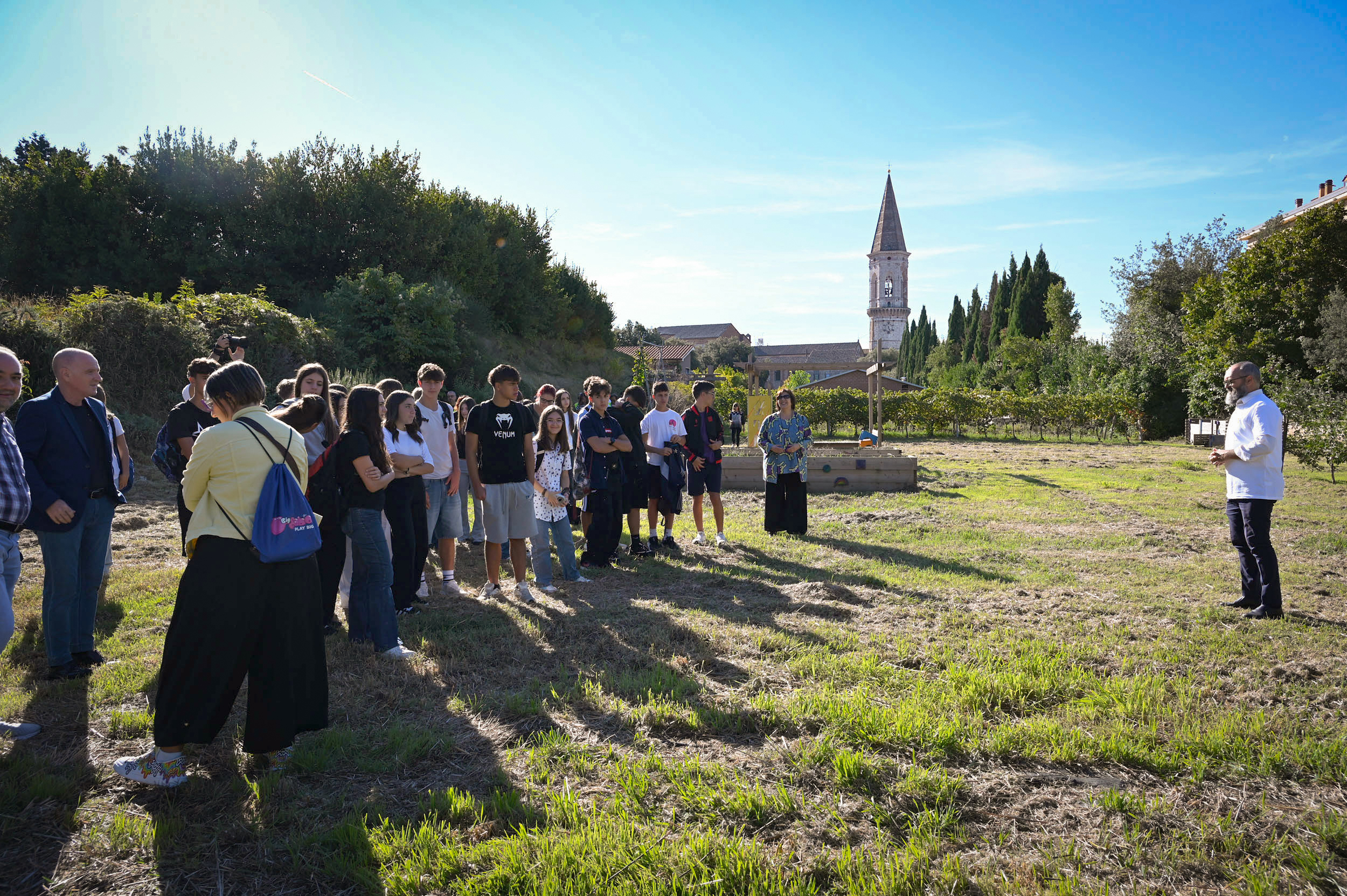 Group in a field listening to a man, church in background